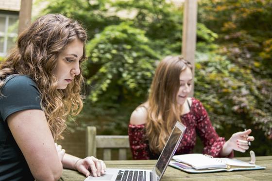 Two Chatham University students sit outside at a bistro table studying independently on their laptops. 