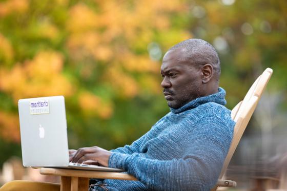 图为一名波胆网站的男学生在外面用笔记本电脑工作, 以秋叶为背景.