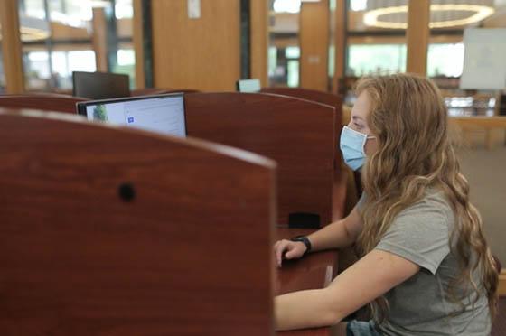 图为英国波胆网站的一名女学生戴着口罩，在图书馆的电脑前工作