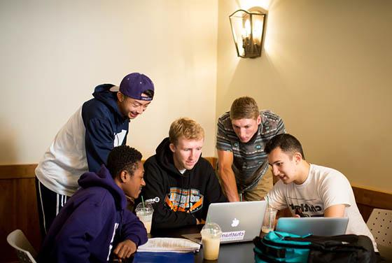 Photo of a group of male Chatham University students huddled around a few laptops and working toge的r