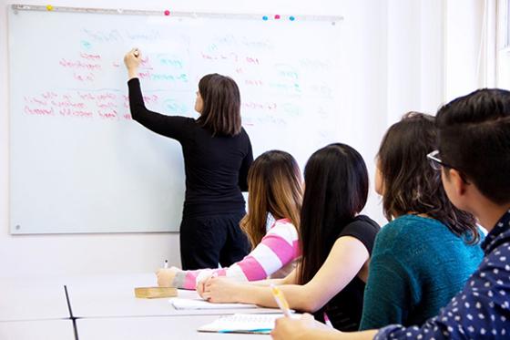 Photo of students watching a professor write notes on a whiteboard. 