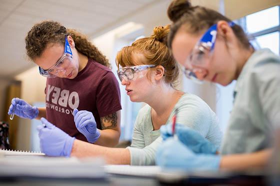 图为三名波胆网站的女学生戴着护目镜和手套在实验室工作