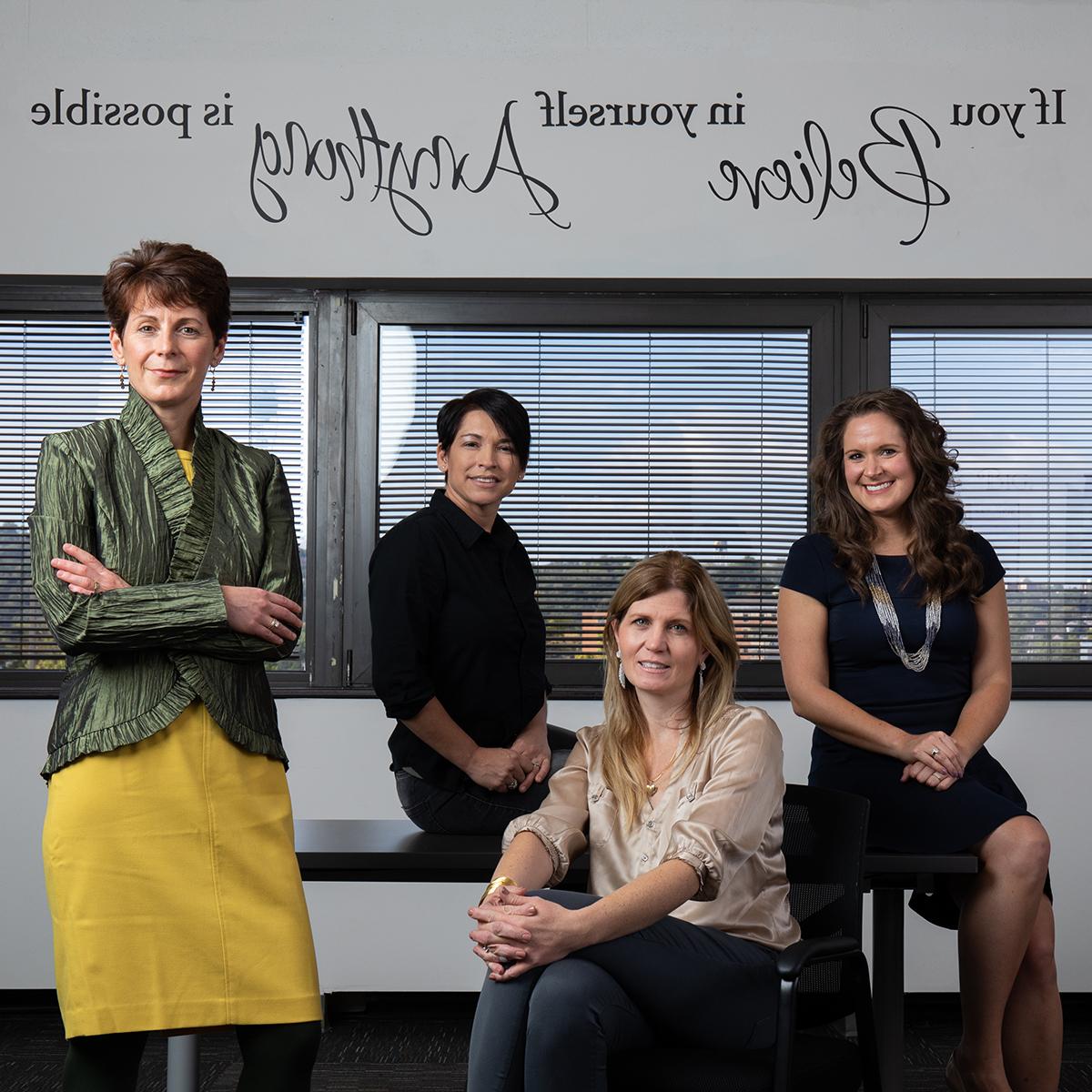 这张照片是四个穿着职业装的女人在写着这句话的墙前摆姿势, “如果你相信自己，一切皆有可能”